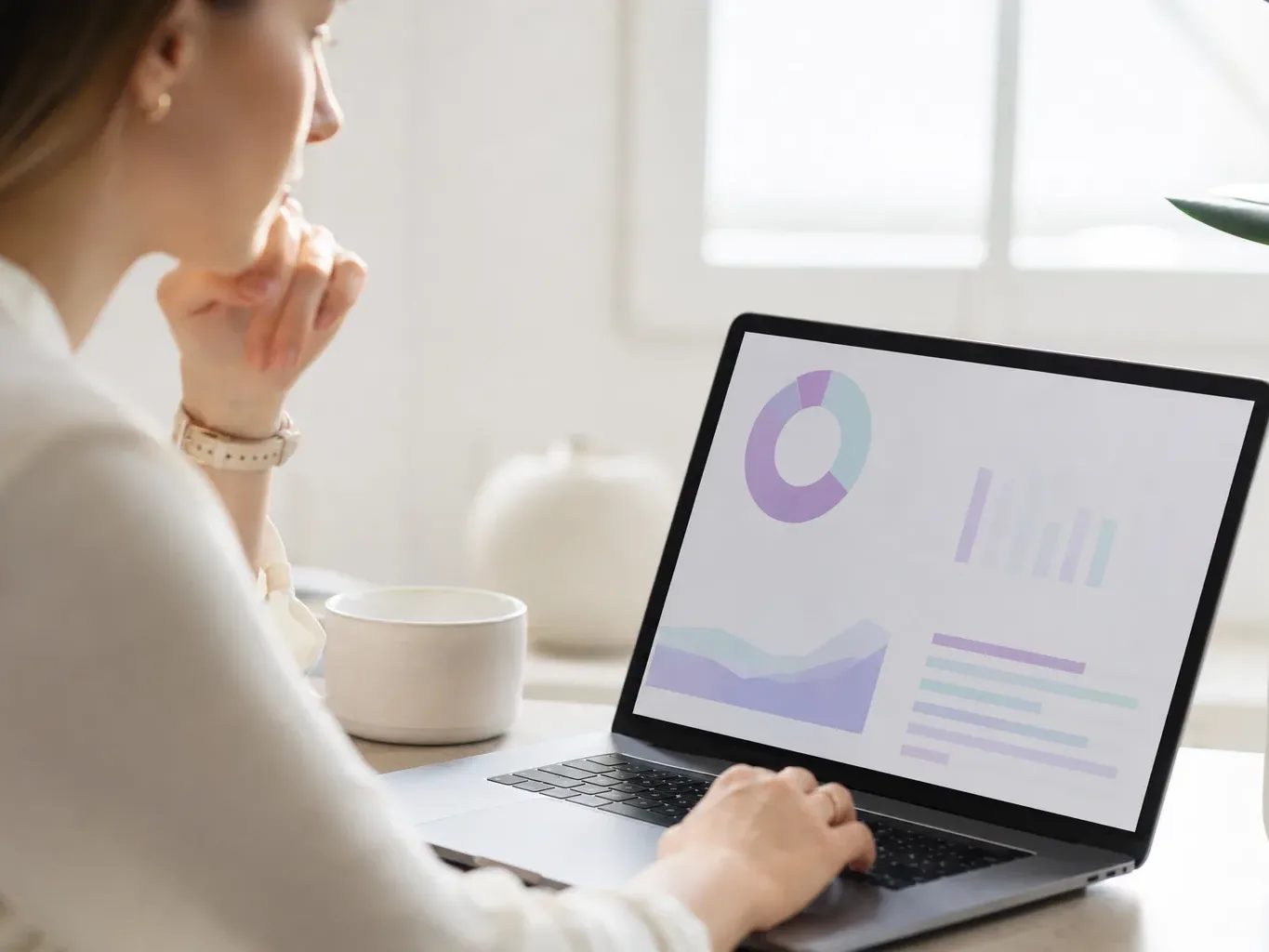 A person sits at a desk viewing a data dashboard with charts on a laptop screen, with a cup nearby